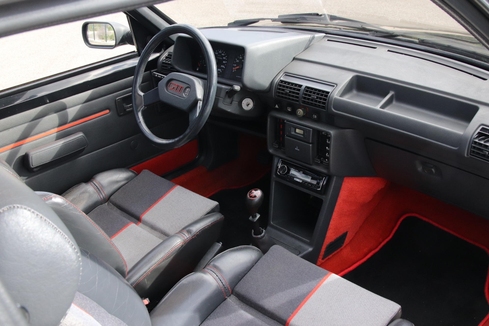 Tableau de bord de Peugeot 205 GTI vu côté passager, moquette rouge et sellerie d'origine