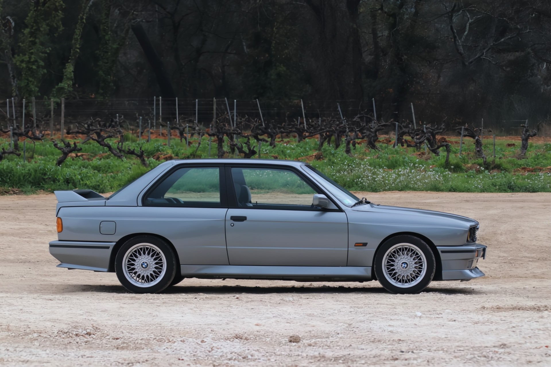 BMW M3 E30 profil devant des vignes