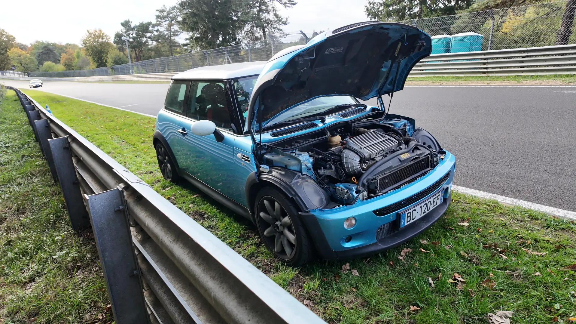 Mini Cooper S R53 bleue arrêtée capot ouvert derrière les rails de la Nordschleife