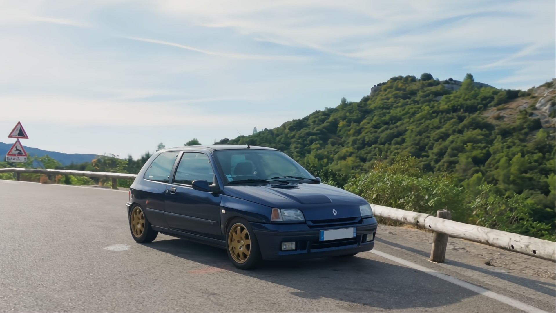 Renault Clio Williams bleue, trois-quarts avant, sur une route de montagne