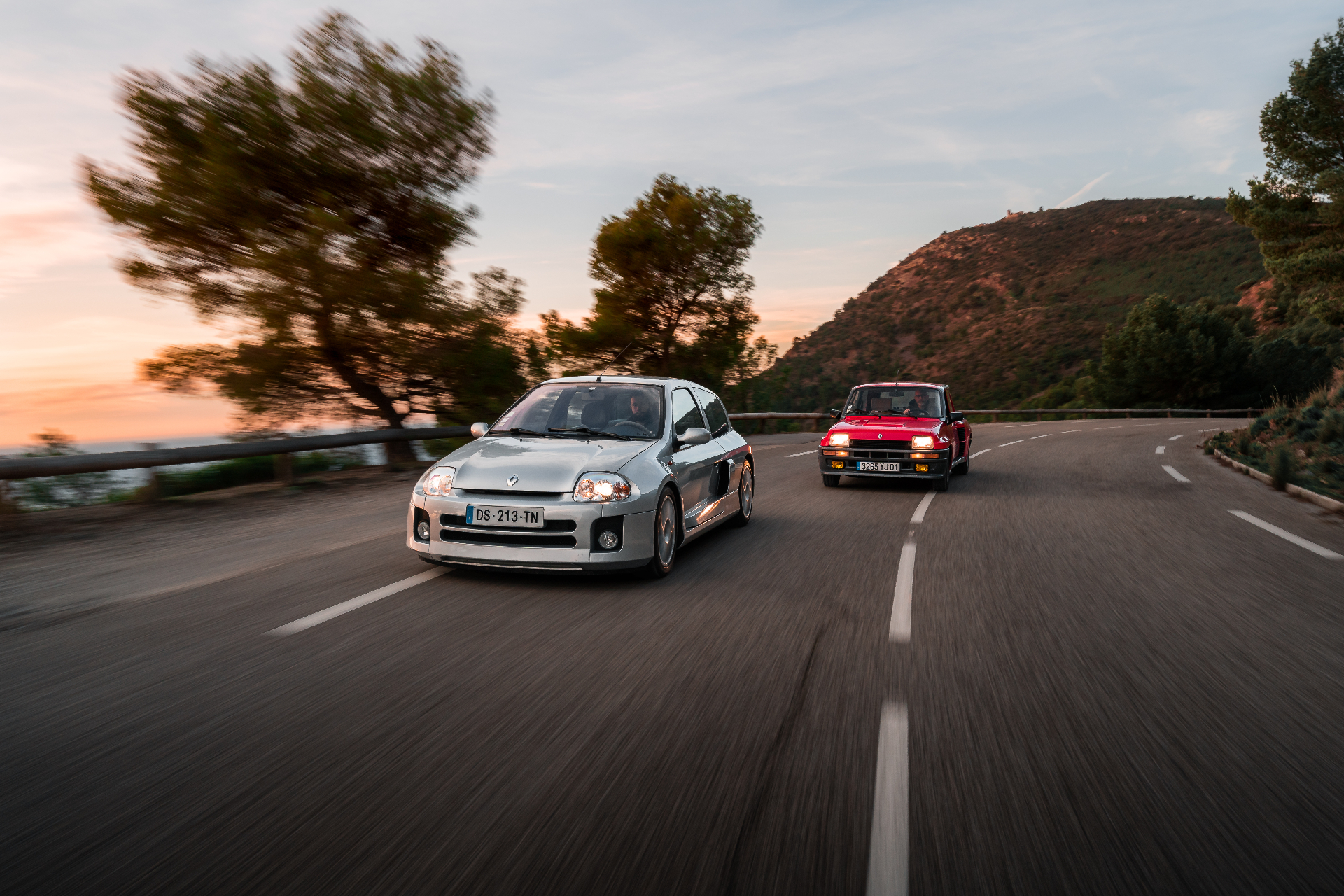 Clio V6 et Renault 5 Turbo sur route côtière au coucher du soleil