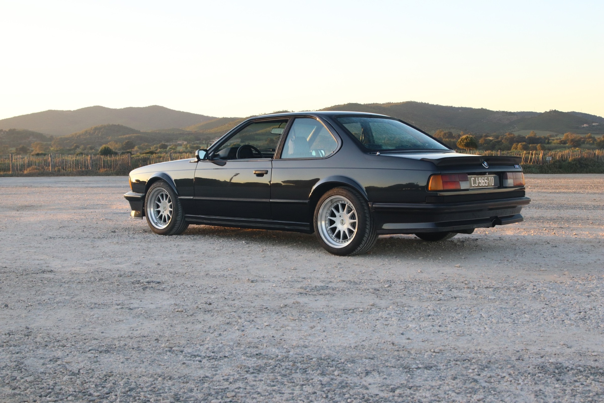 BMW M635 CSi noire de trois-quarts arrière, vue depuis la gauche, montagnes en fond