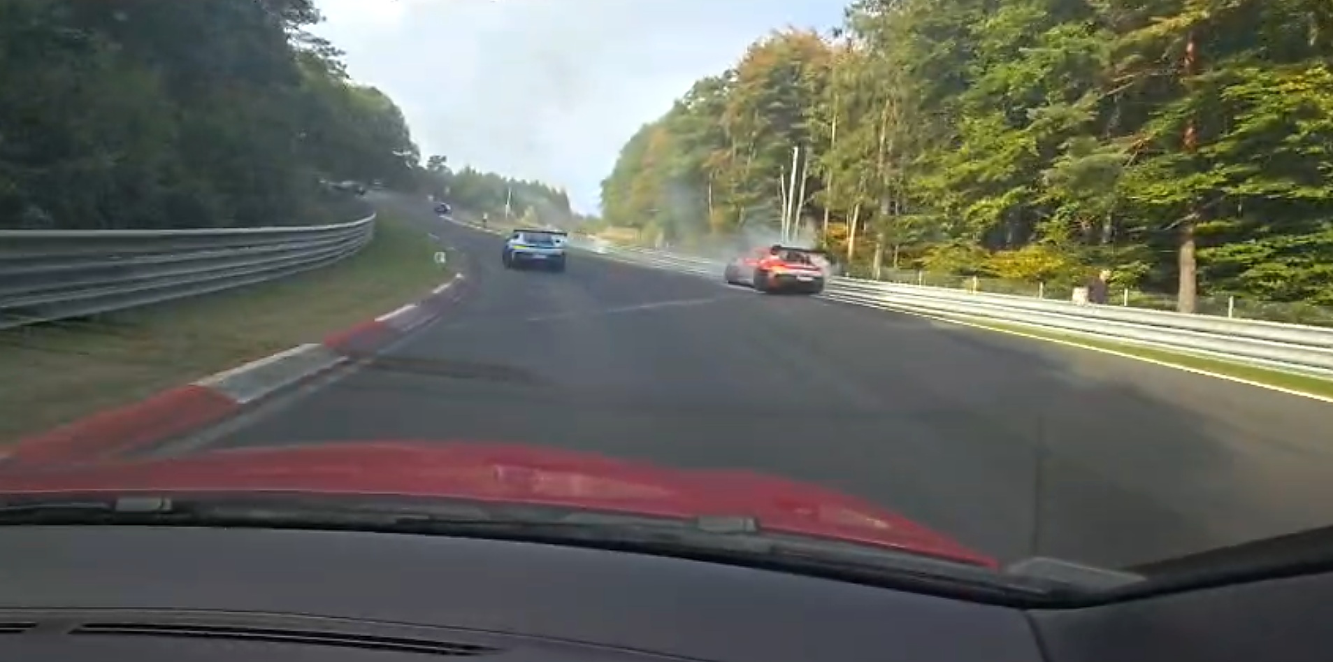 Porsche 911 GT3 rouge près du rail de la Nordschleife avec de la fumée visible