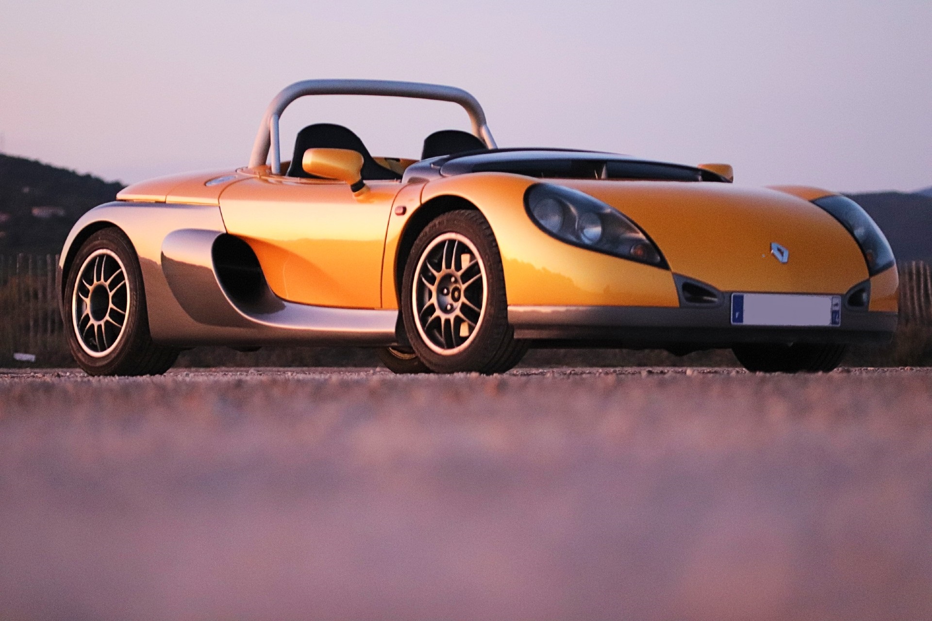 Renault Spider jaune et gris de profil trois-quarts au coucher du soleil