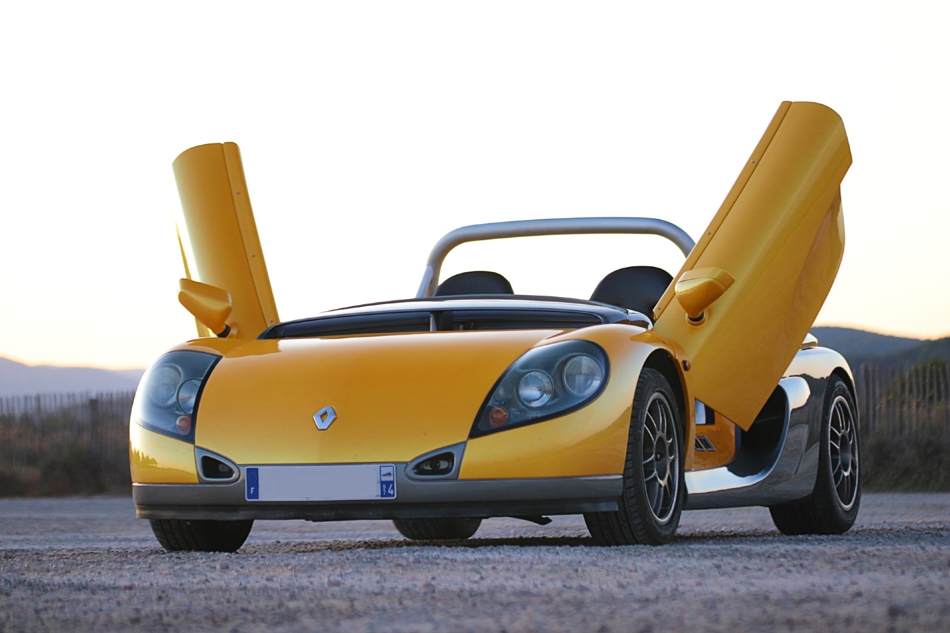 Renault Spider jaune portes papillon ouvertes vu de face au coucher du soleil
