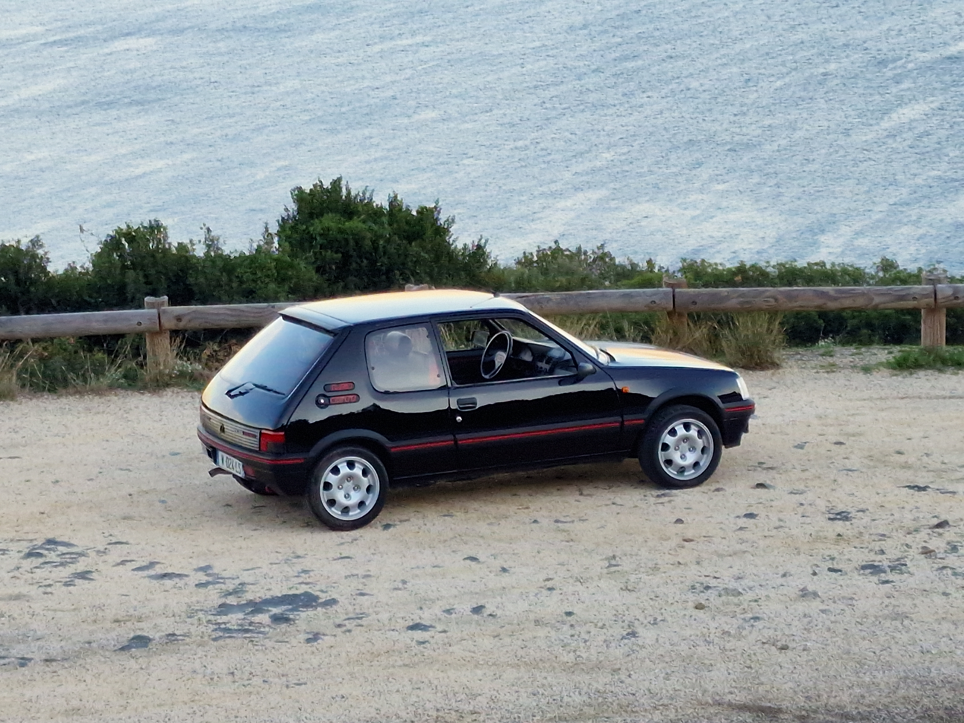 Peugeot 205 GTI noire de profil au bord de la mer
