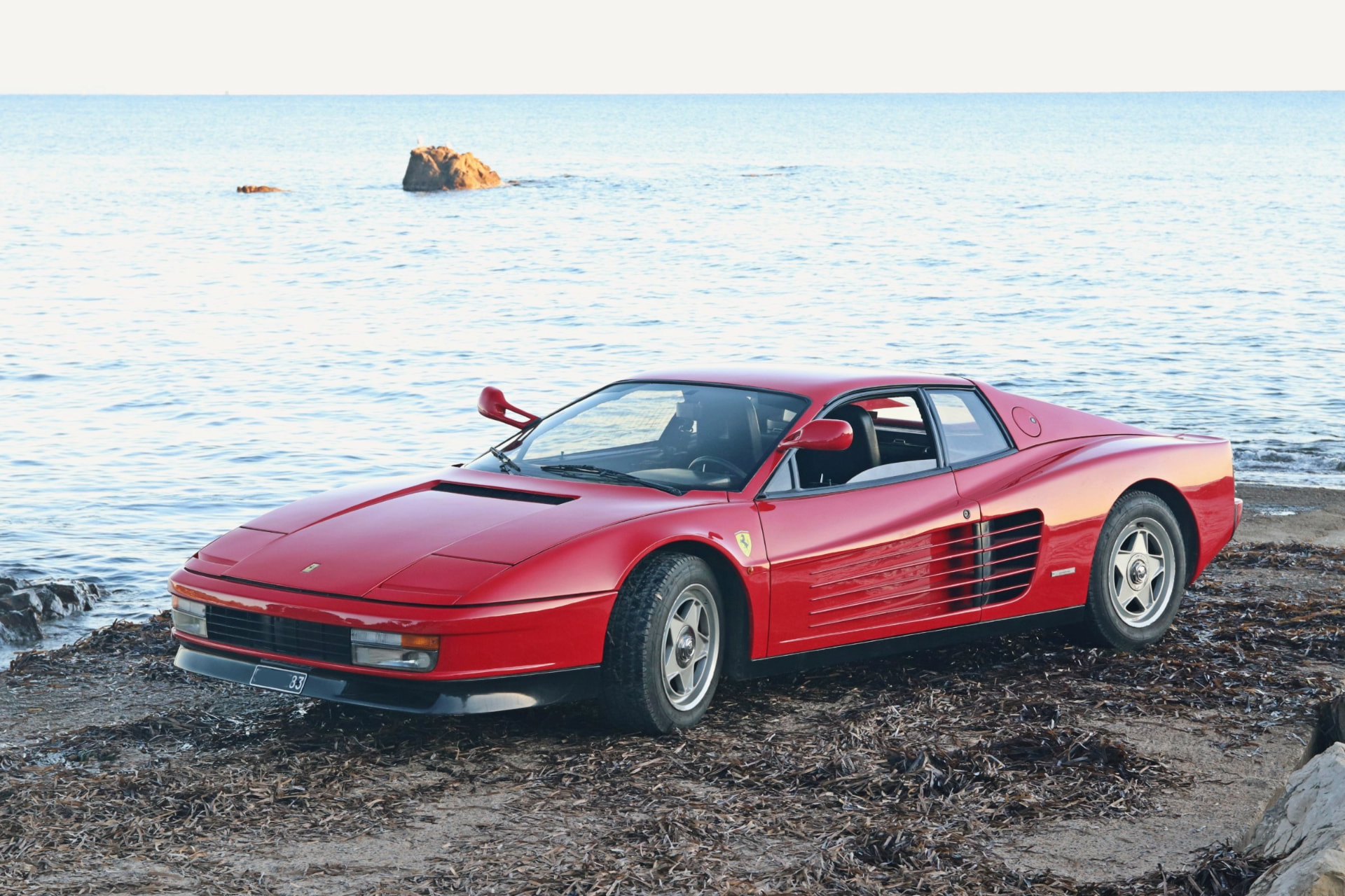 Ferrari Testarossa rouge de trois quarts avant au bord de la mer