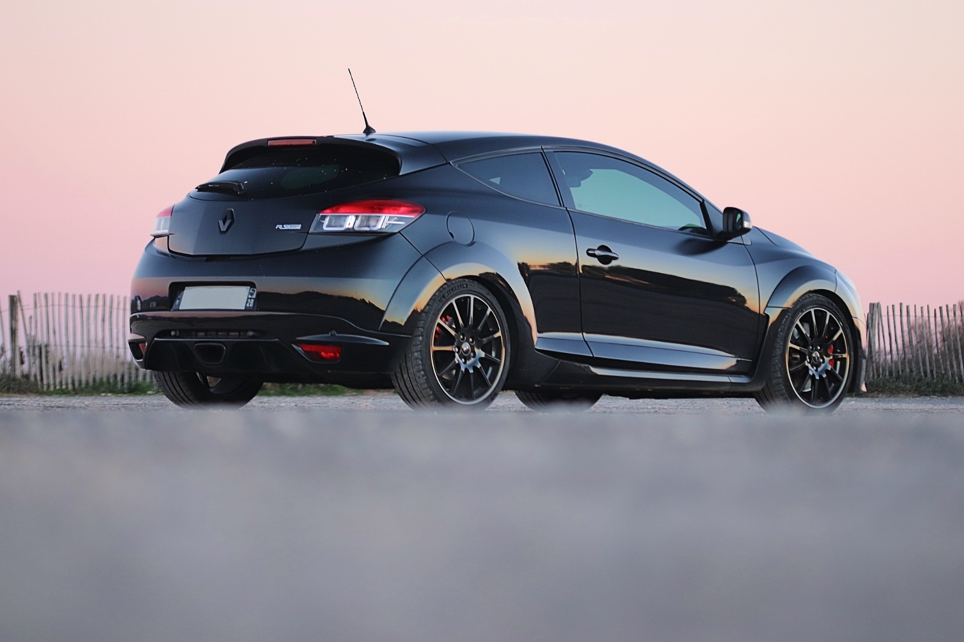 Renault Mégane 3 RS noire de trois quarts arrière avec spoiler et double sortie d'échappement au coucher du soleil