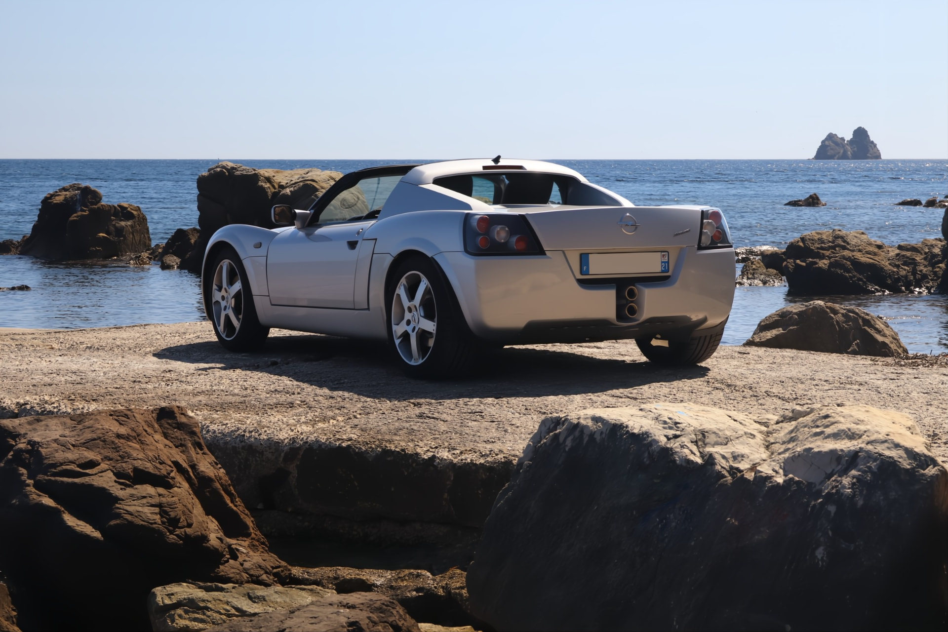 Opel Speedster argent vu de l'arrière sur les rochers face à la mer