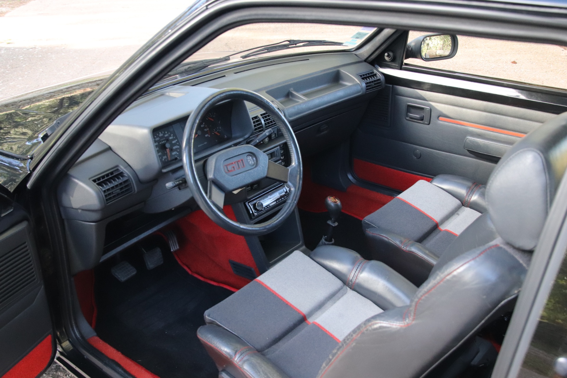 Intérieur de Peugeot 205 GTI : volant GTI, sellerie tissu gris à liserés rouges et moquette rouge