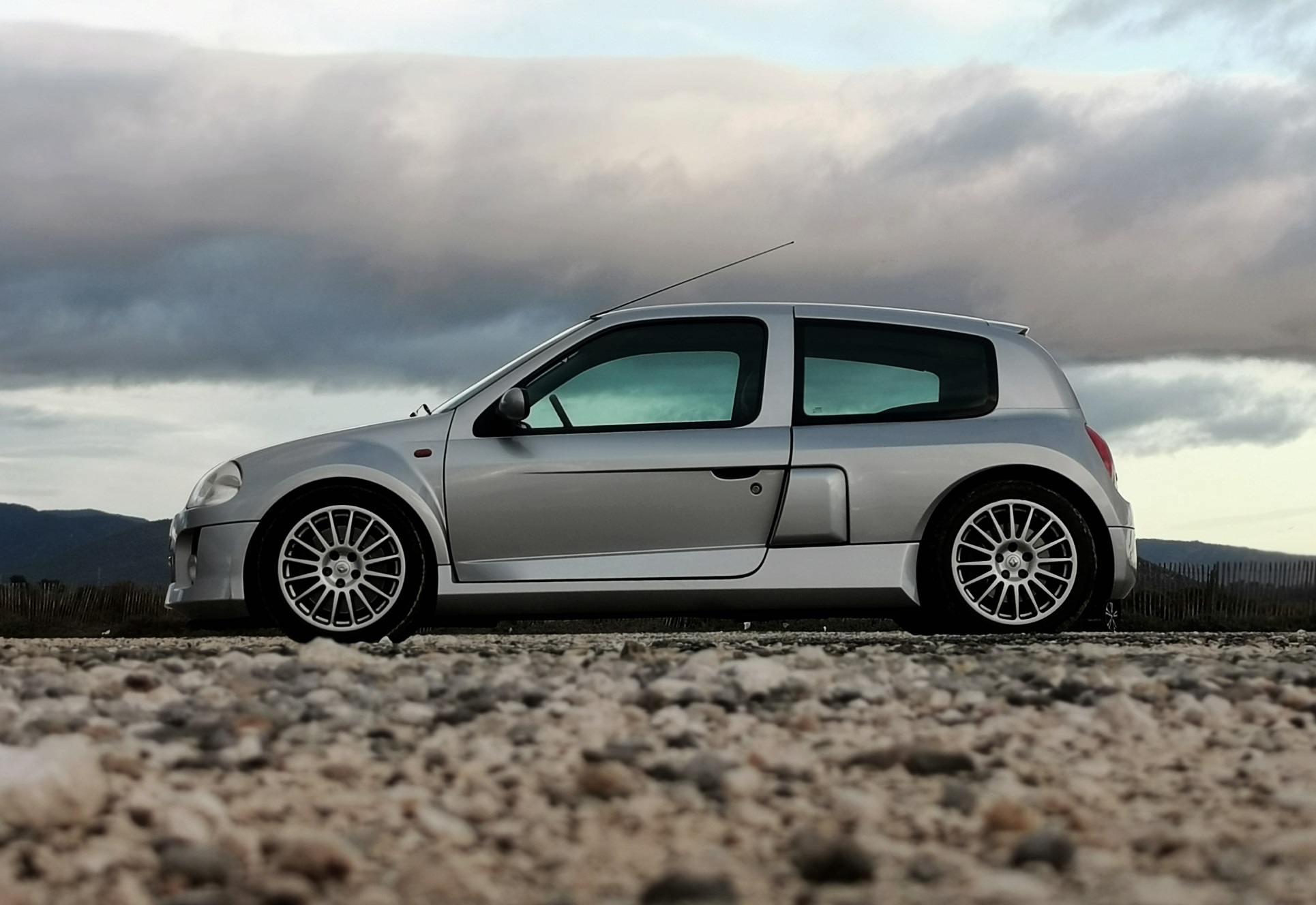 Renault Clio V6 grise de profil sur un chemin de gravier
