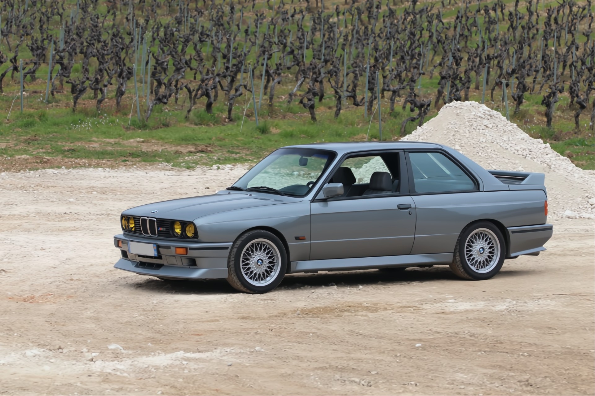BMW M3 E30 grise devant un vignoble