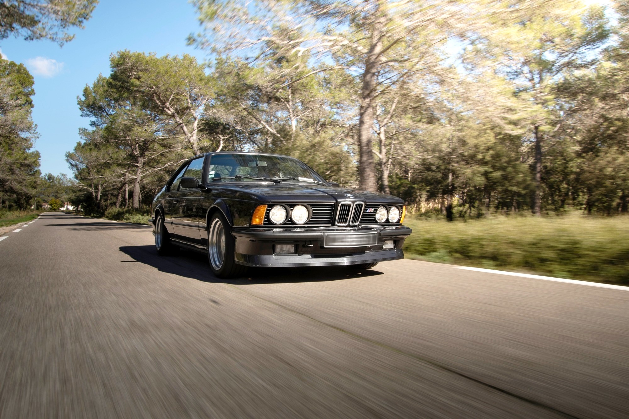 BMW M635 CSi noire en mouvement vue de trois-quarts avant sur une route provençale