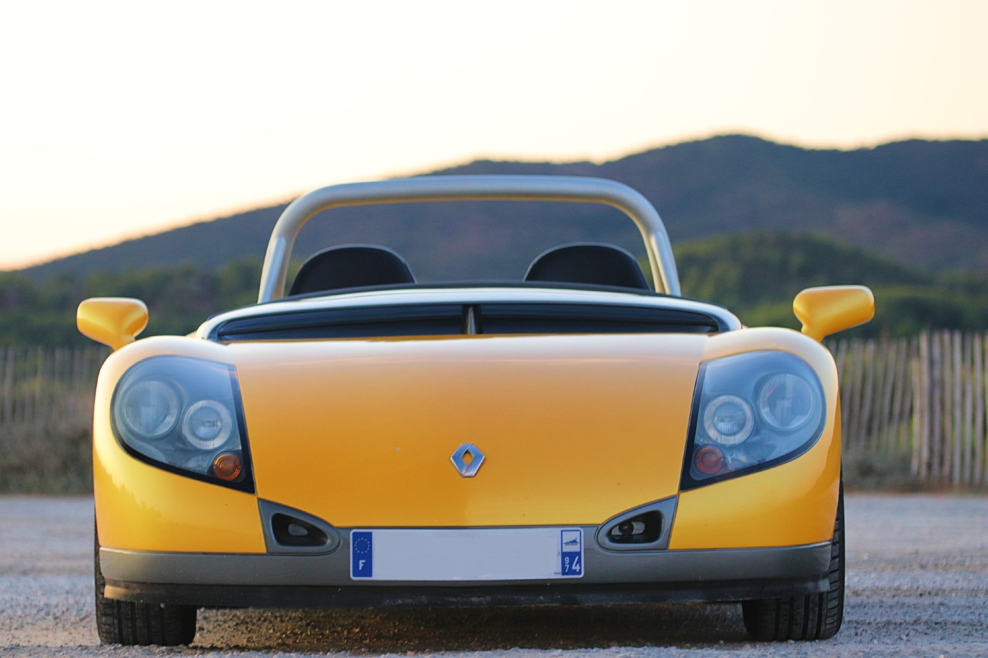 Renault Spider jaune vu de face, phares ronds et logo Renault centré, au coucher du soleil