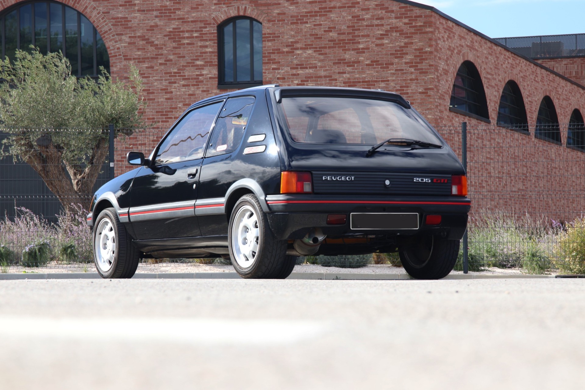 Peugeot 205 GTI 1.9 noire vue de trois quarts arrière devant un bâtiment en brique