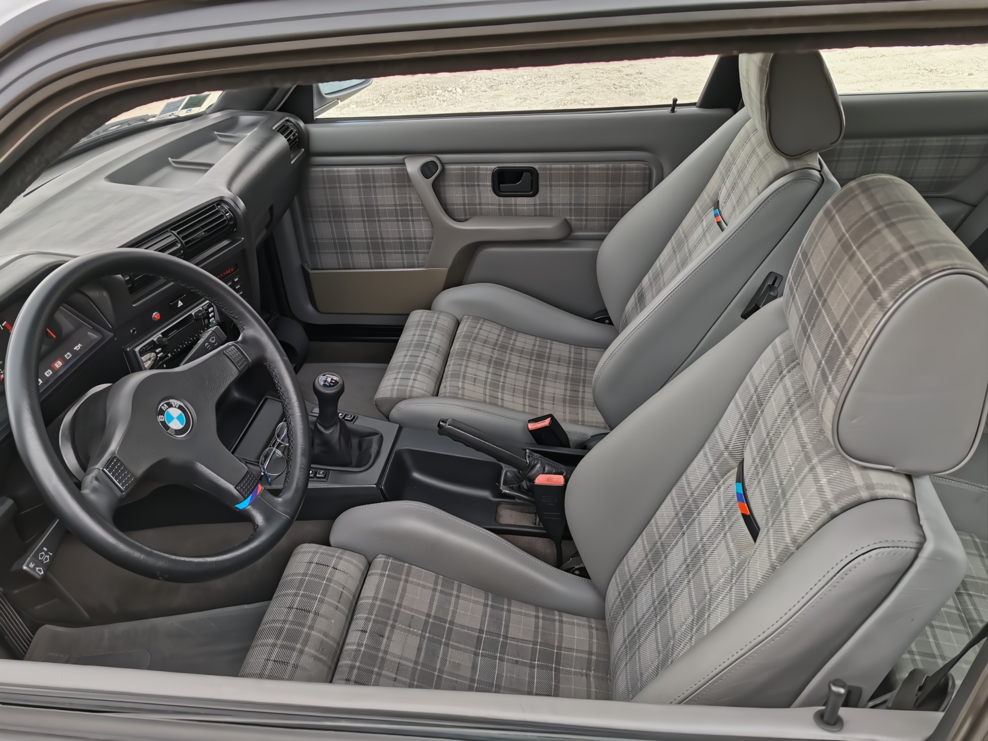 Intérieur BMW M3 E30 avec sièges à carreaux, volant M et levier court