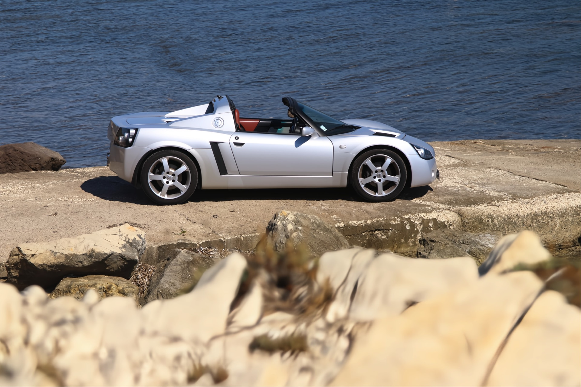 Opel Speedster argent de profil au bord de l'eau, capote ouverte