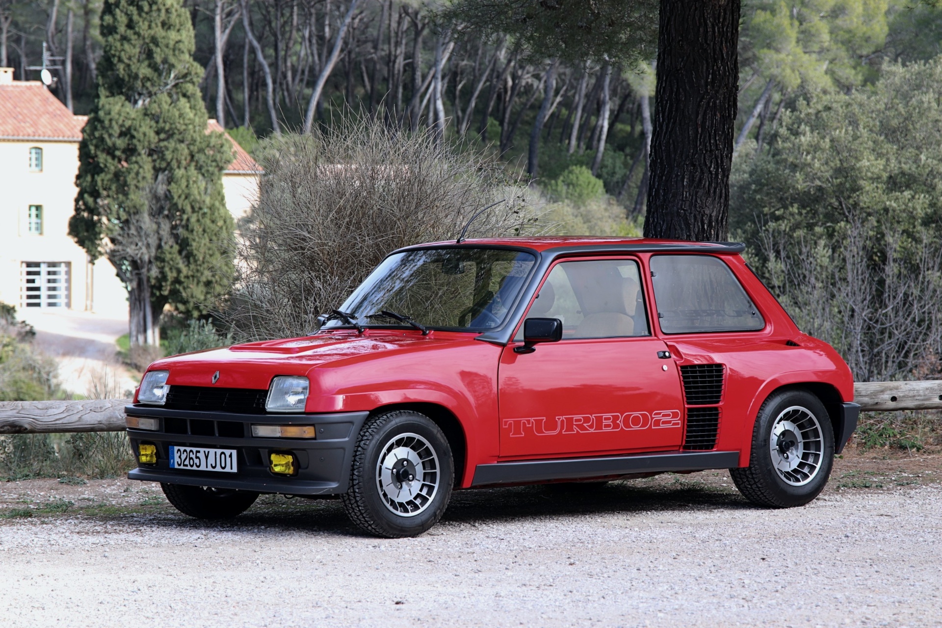 Renault R5 Turbo 2 rouge, trois-quarts avant, garée devant une bastide provençale