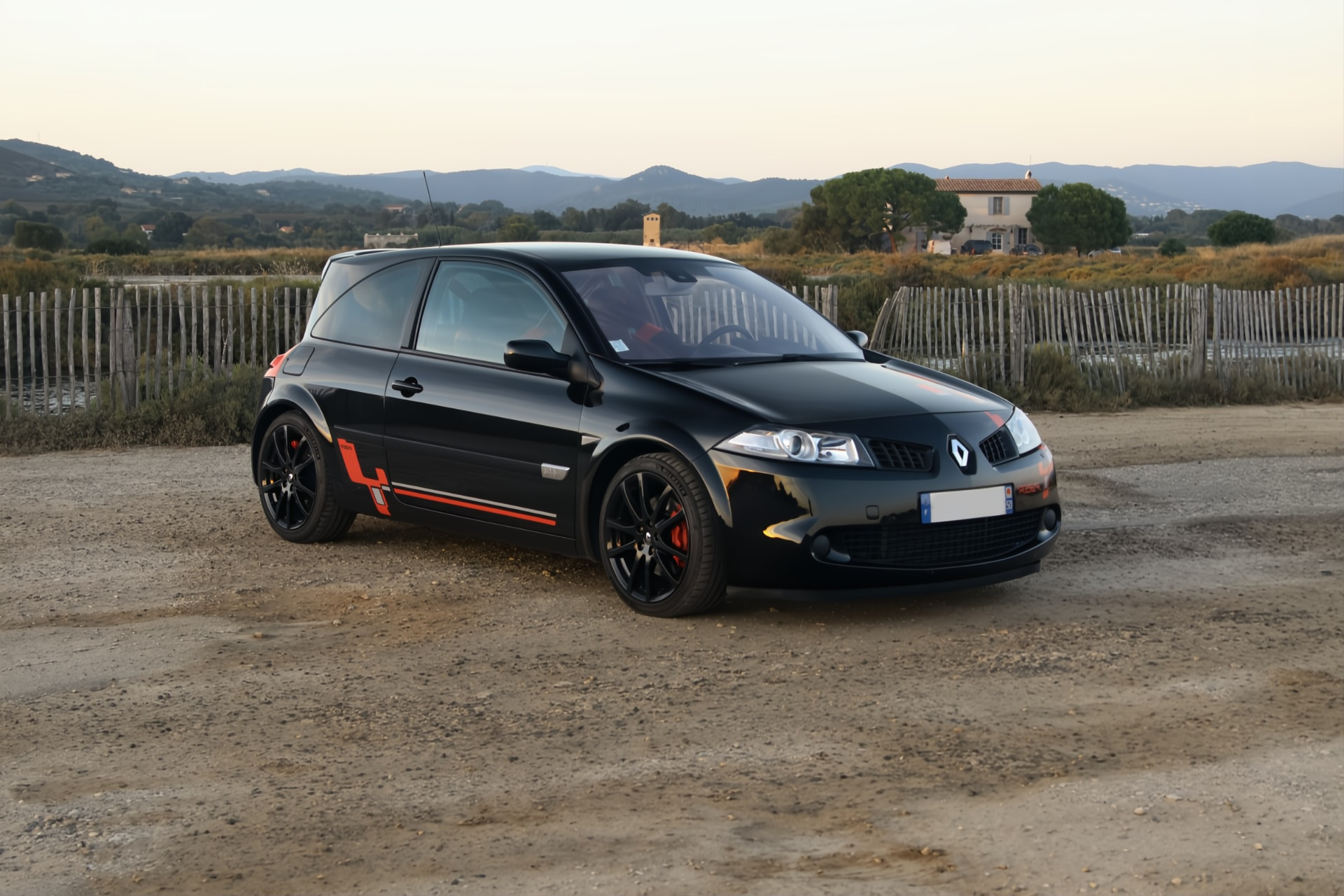 Renault Mégane R26.R noire de trois quarts avant sur une route au coucher du soleil