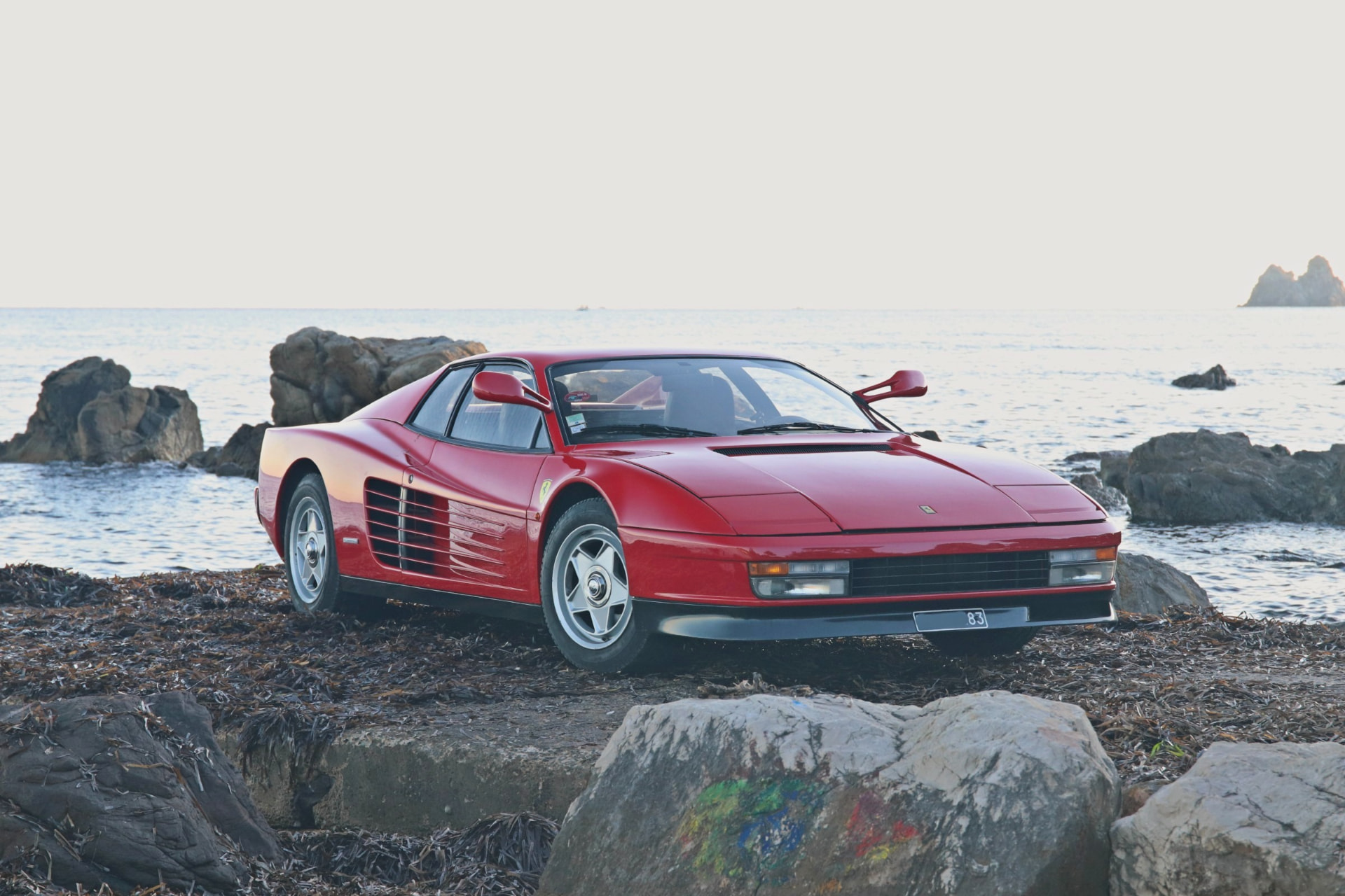 Ferrari Testarossa rouge de face au bord de l’eau au coucher du soleil