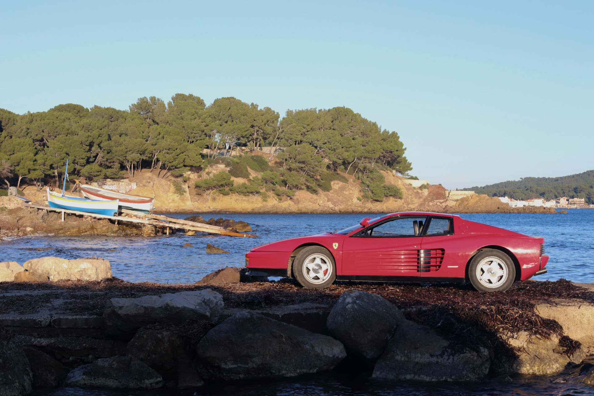 Profil d’une Ferrari Testarossa rouge devant une calanque